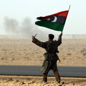 A rebel fighter holds a Kingdom of Libya flag and a knife in a battle near Ras Lanuf