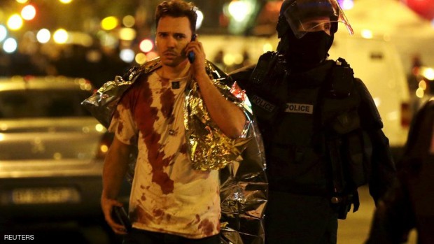 A French policeman assists a blood-covered victim near the Bataclan concert hall following attacks in Paris, France