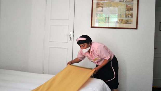 An hotel maid works wearing a mask, tryi